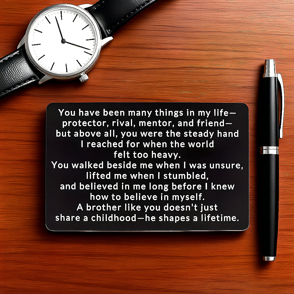 Black engraved metal wallet card reading 'A Brother Shapes A Lifetime' lying on a brown wooden table next to a black wristwatch and pen.