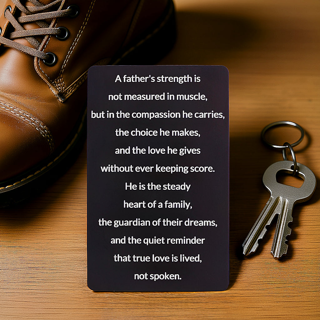 Black engraved metal wallet card with a message about a father's strength and compassion, lying on a wooden table next to a brown leather boot and a set of keys.