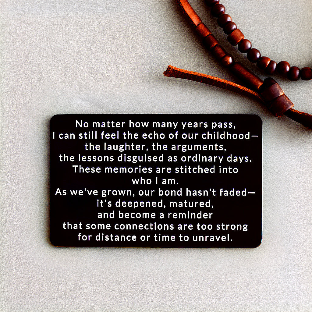 Black engraved metal wallet card reading 'Our Bond Deepened Beyond Childhood' next to a leather necklace with brown beads.