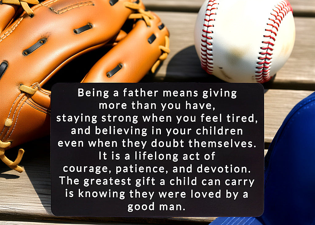 Black engraved metal wallet card with a message about being loved by a good father, lying on a wooden bench next to a baseball glove, baseball, and blue cap.