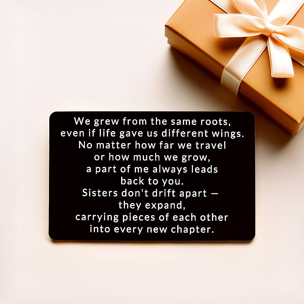Black engraved metal wallet card reading 'We Grew From the Same Roots' lying on a cream background next to a gold gift box with a satin bow.