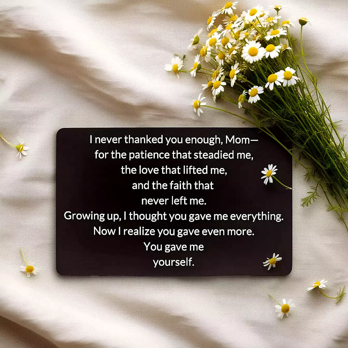 Black engraved metal wallet card reading 'You Gave Me Yourself' lying on white linen next to wildflowers.