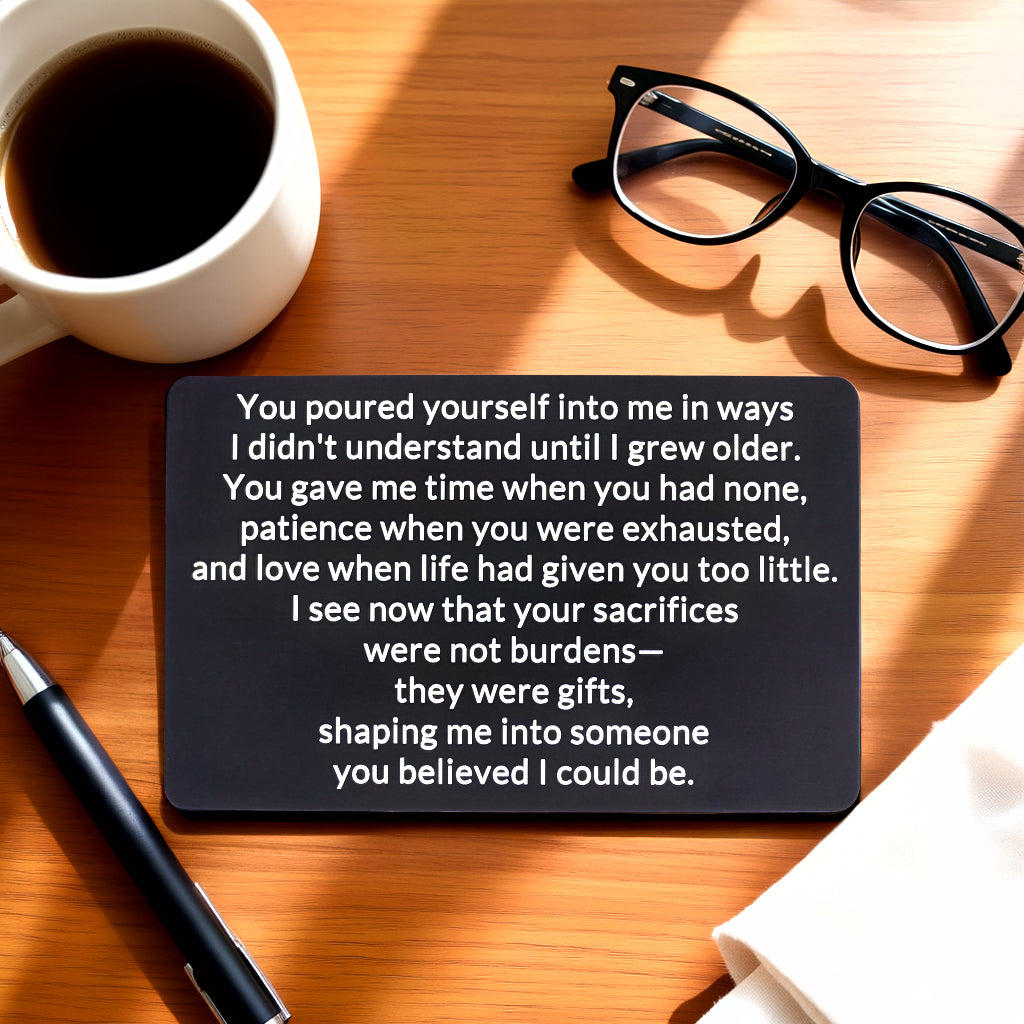 Black engraved metal wallet card reading 'Your Sacrifices Were Gifts' on a coffee table beside a coffee cup.
